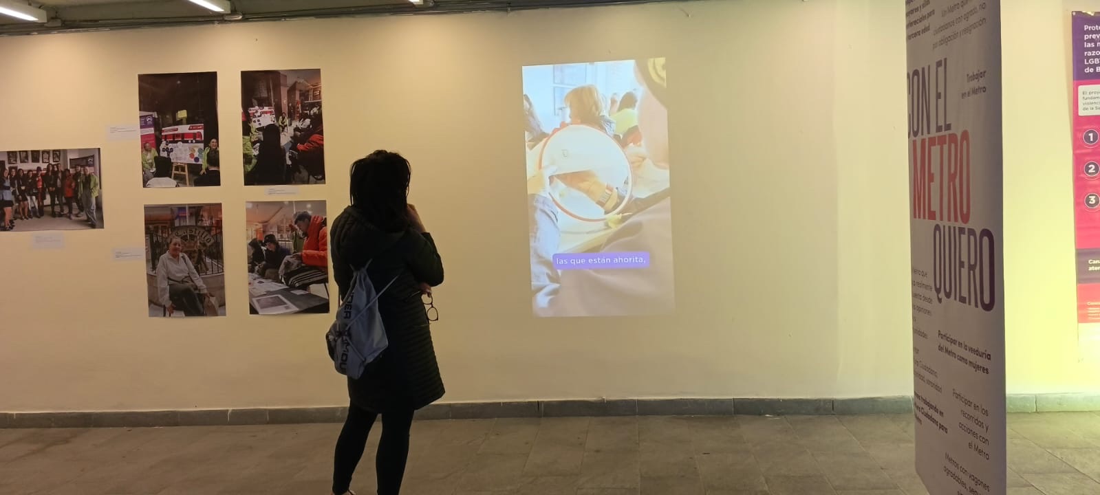 En el fondo: una pared con fotos y una proyección de video beam. Al frente una mujer que está viendo lo que se está proyectando