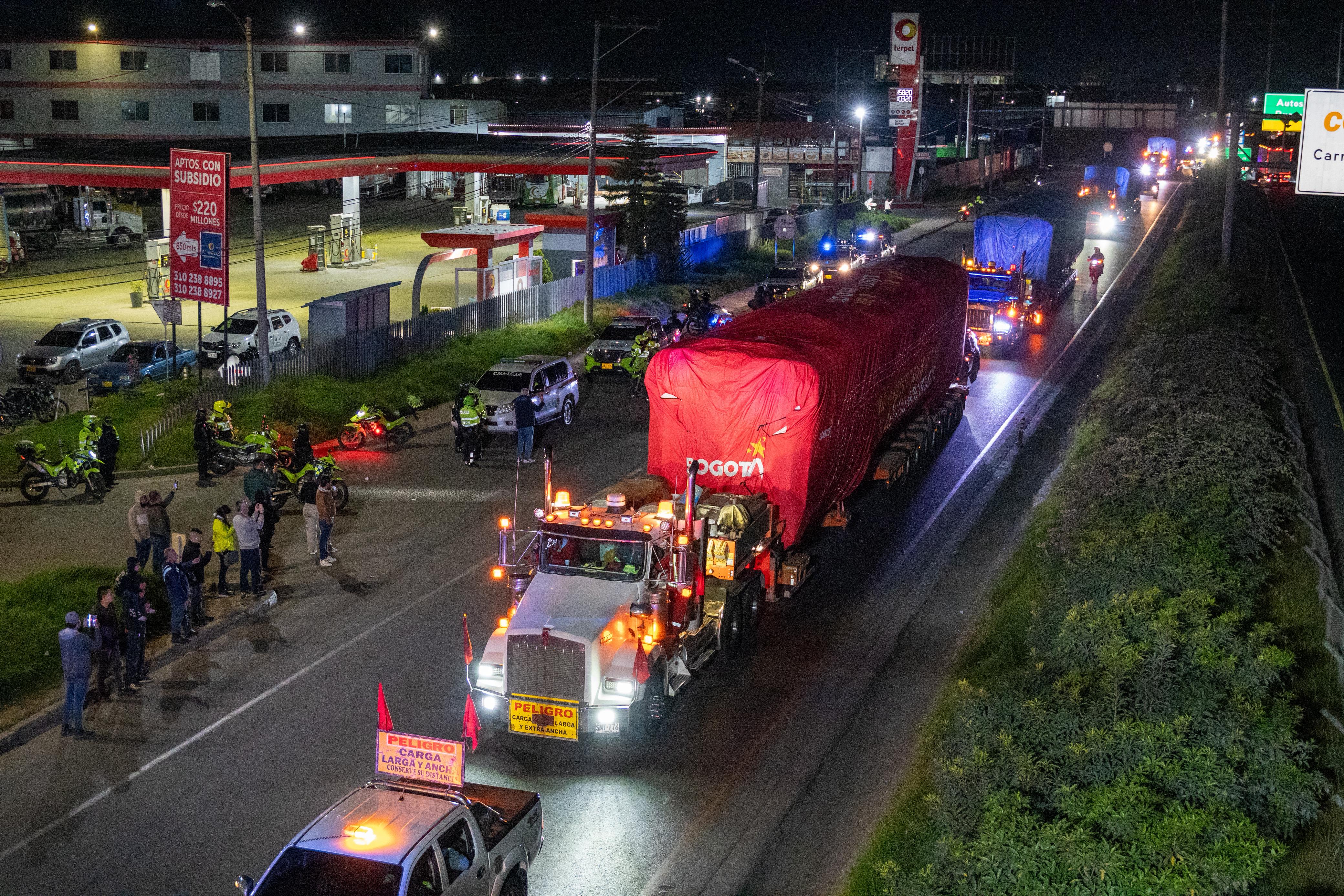 El vagón cubierto con una funda roja, sobre la camabaja que viene en caravana por las calles de Bogotá, escoltado por policías y muchos ciudadanos tomando fotos.