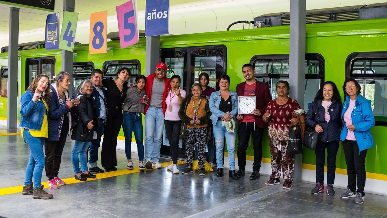 Un gestor social de la Empresa Metro posa sonriendo con los 34 vendedores informales en frente del Vagón del Metro de Bogotá