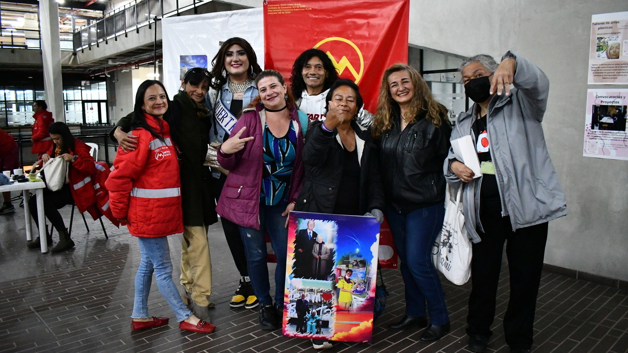 Personas abrazadas y sonriendo frente a un pendón del Metro