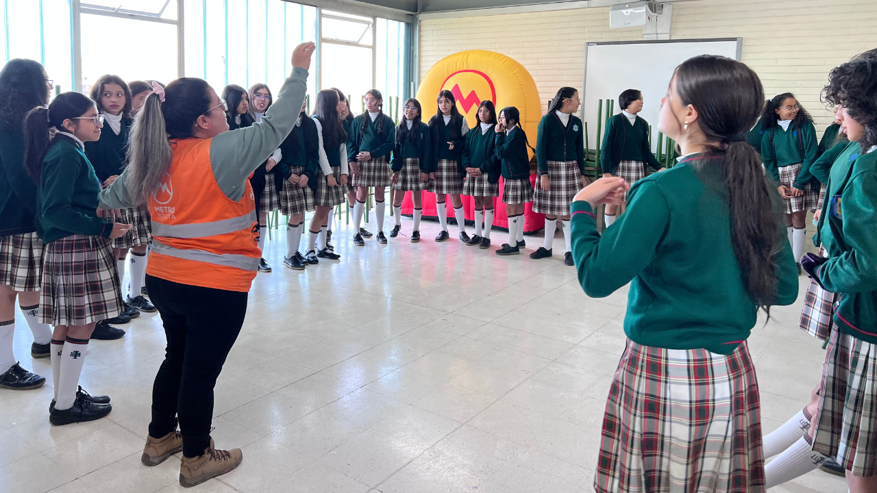 Foto de trabajadora del metro dando instrucciones a estudiantes de colegio